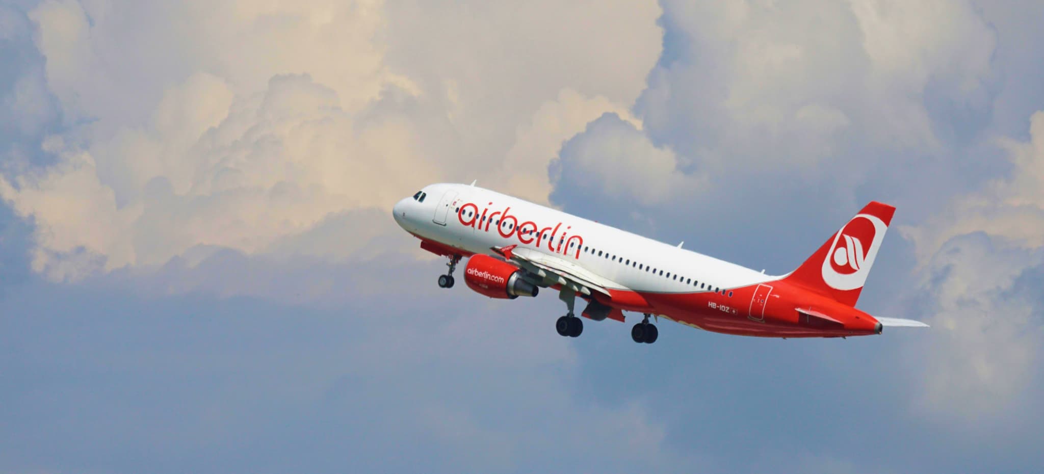 A red and white Air Berlin airplane ascends against fluffy, dramatic clouds, symbolizing freedom and travel.